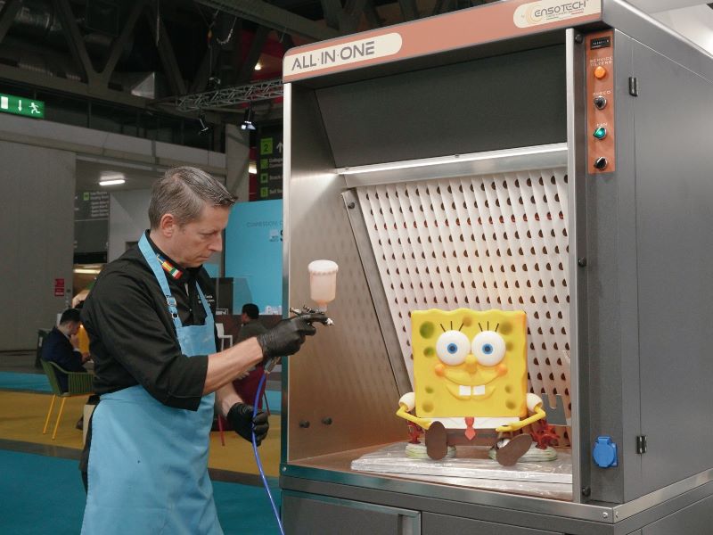 Cabina aspirante All In One Ensotech&trade; con torta SpongeBob decorata a spray al burro di cacao in fiera Host Milano.