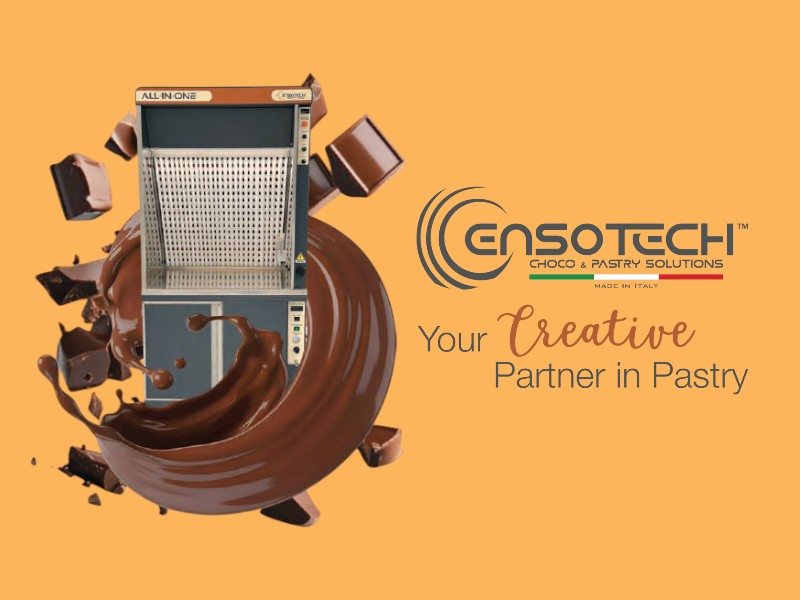 Cabina di aspirazione e filtrazione per pasticceria All In One Ensotech circondata da splash di cioccolato e blocchi di cioccolato in volo su sfondo arancione.