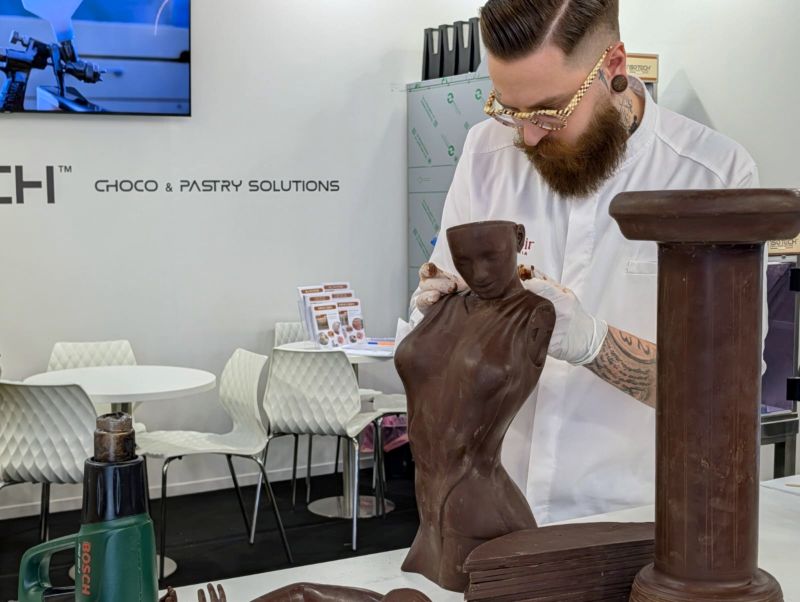 Chef esperto rifinisce a mano una scultura di cioccolato artistica utilizzando tecniche di pasticceria professionale.